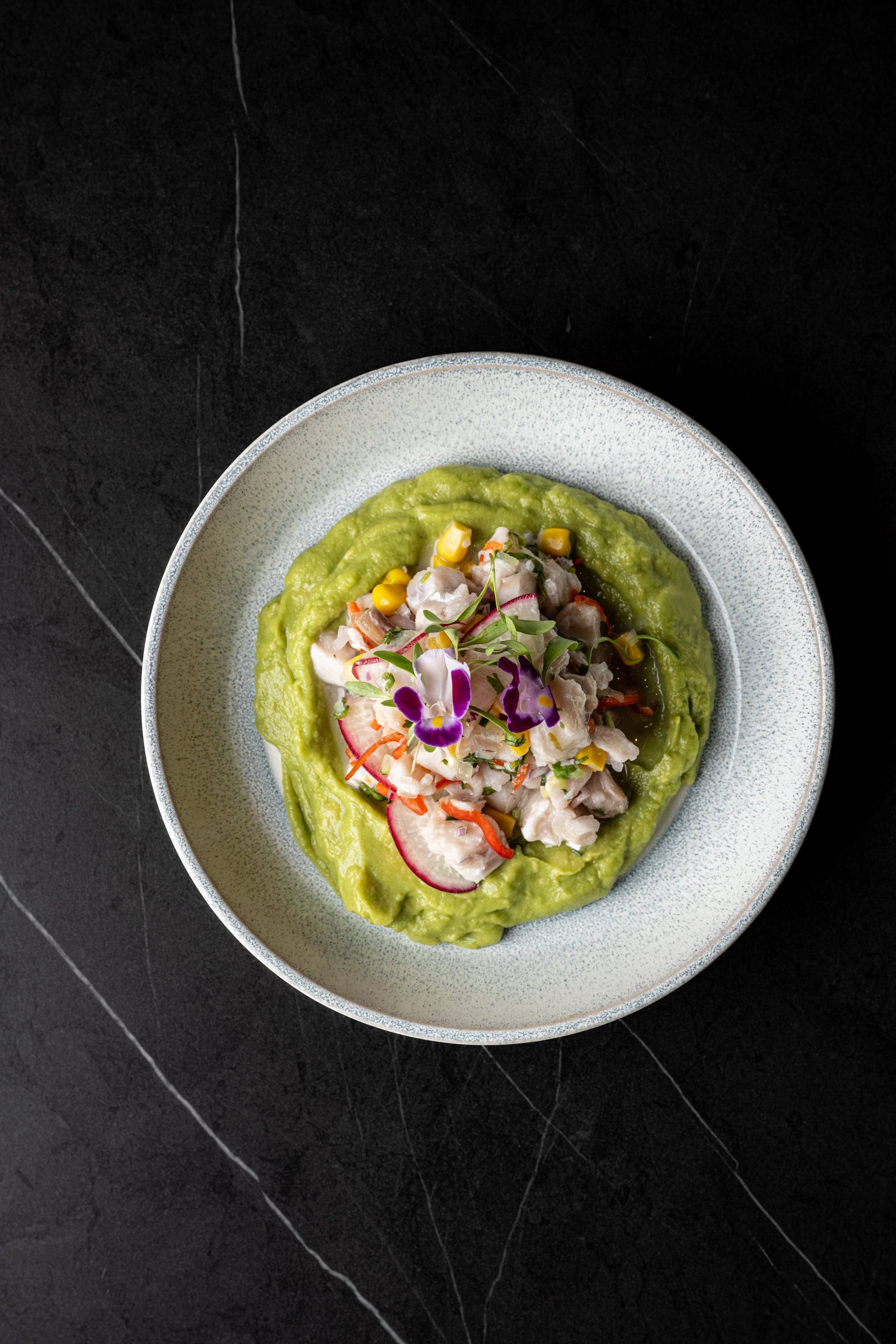 Ceviche sobre crema de aguacate con maíz, rábano y flores